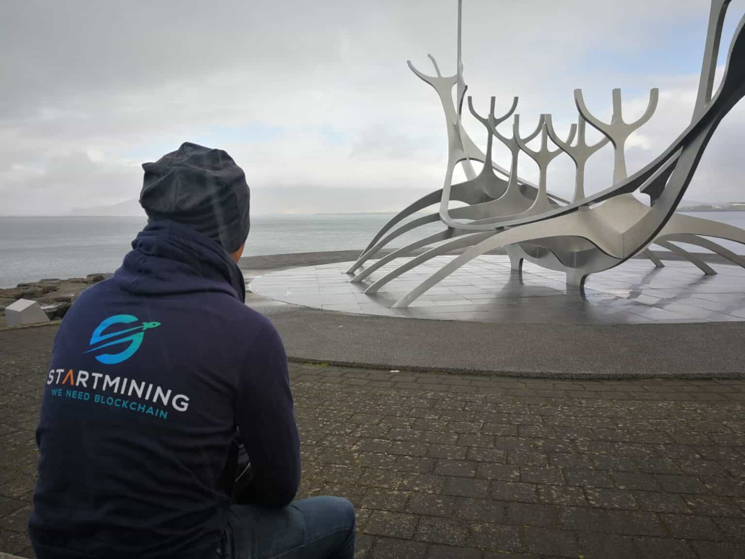 EmployÃƒÂ© de StartMining en Islande, devant une sculpture emblÃƒÂ©matique, marquant lÃ¢â‚¬â„¢installation de milliers de GPU pour une infrastructure de colocation durable et ÃƒÂ©coÃƒÂ©nergÃƒÂ©tique en septembre 2021.